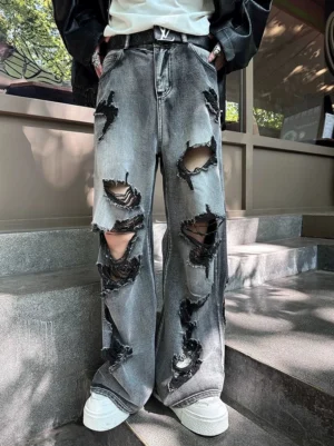Male model wearing distressed gray wide-leg jeans with oversized frayed rips, black leather jacket, white tee, and white sneakers in a Korean punk streetwear outfit