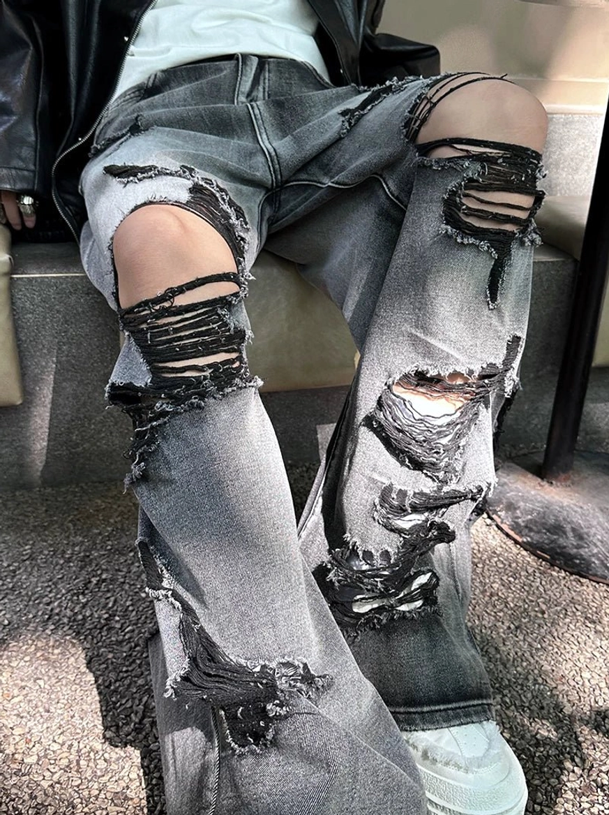 Close-up view of distressed gray denim legs with multiple shredded holes, raw frayed edges, and relaxed wide-leg streetwear fit