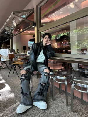 Distressed gray wide-leg jeans with ripped knees and flared hem styled with a black leather jacket and white sneakers in a cafe