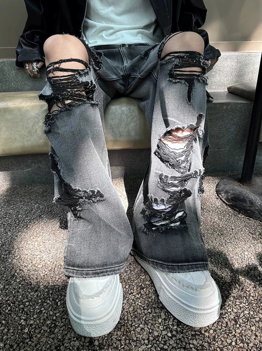 Seated streetwear outfit featuring faded black-gray ripped wide-leg jeans, destroyed thigh details, white tee, and white platform sneakers