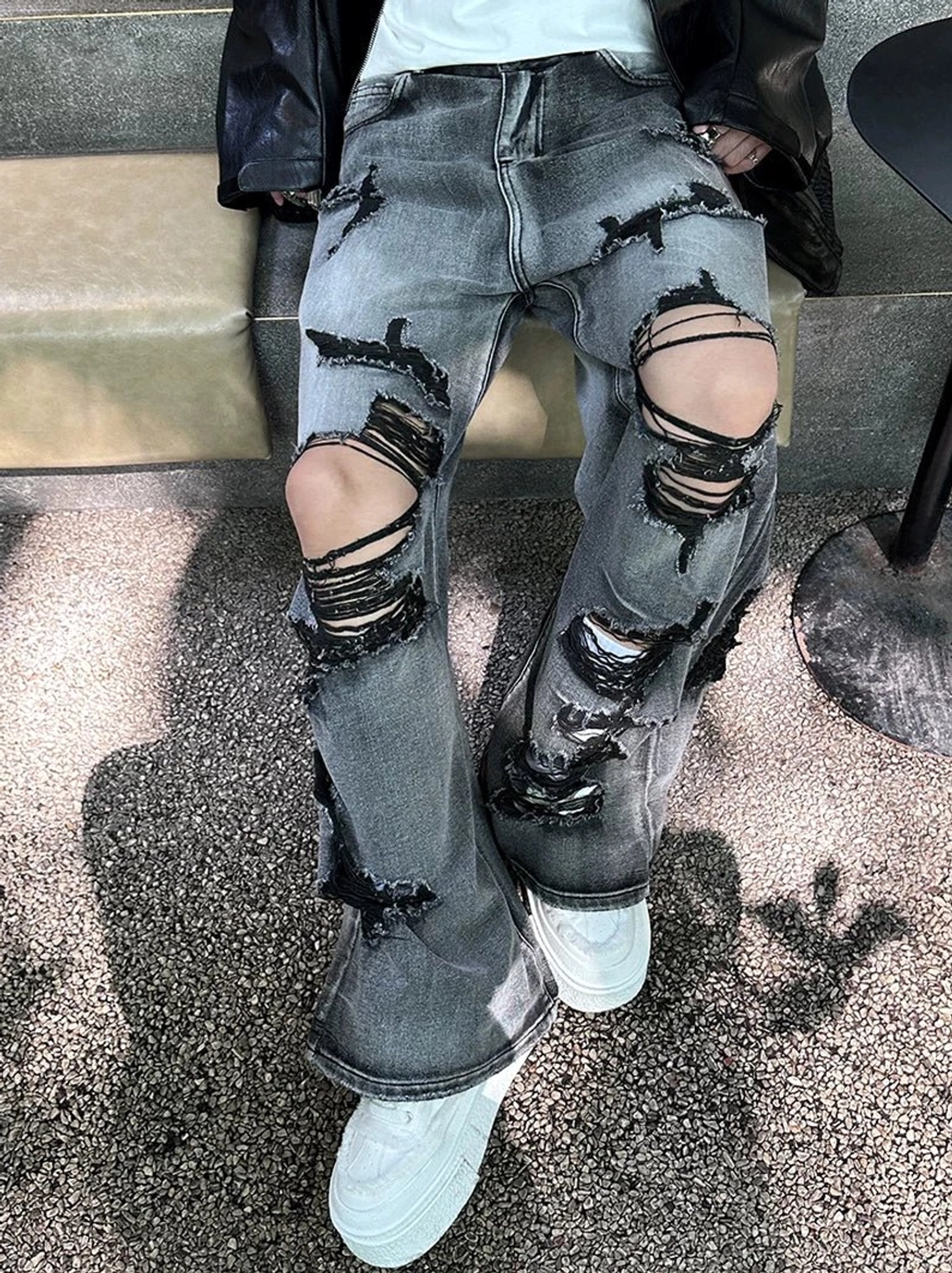 Close-up of black-gray faded wide-leg jeans featuring layered frayed rips across the knees and lower legs in a streetwear outfit