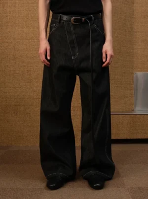 Front full body view of raw black contrast stitch balloon leg denim trousers styled with black belt in studio