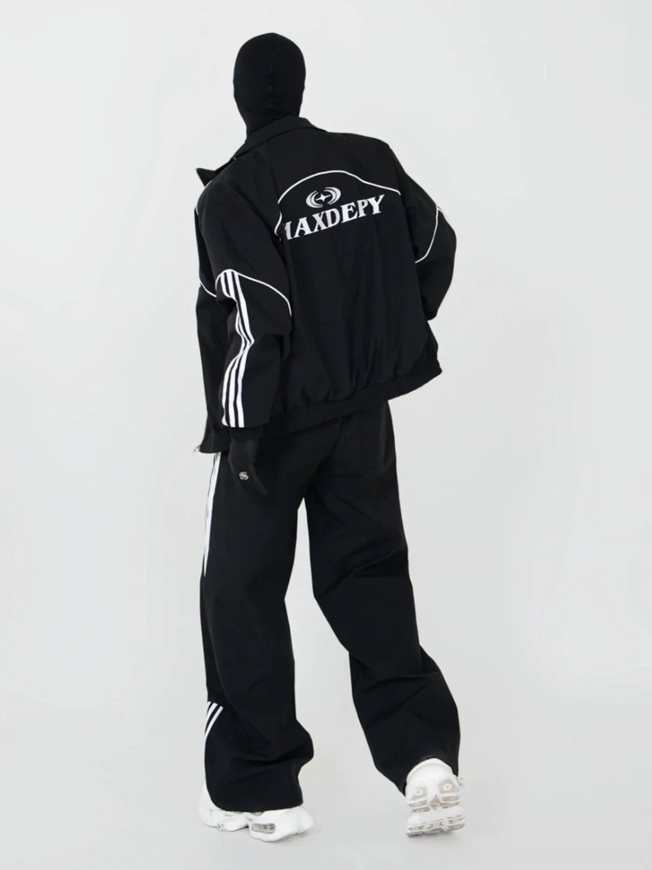 Rear view of black wide-leg triple-stripe track pants with matching streetwear jacket and white chunky sneakers