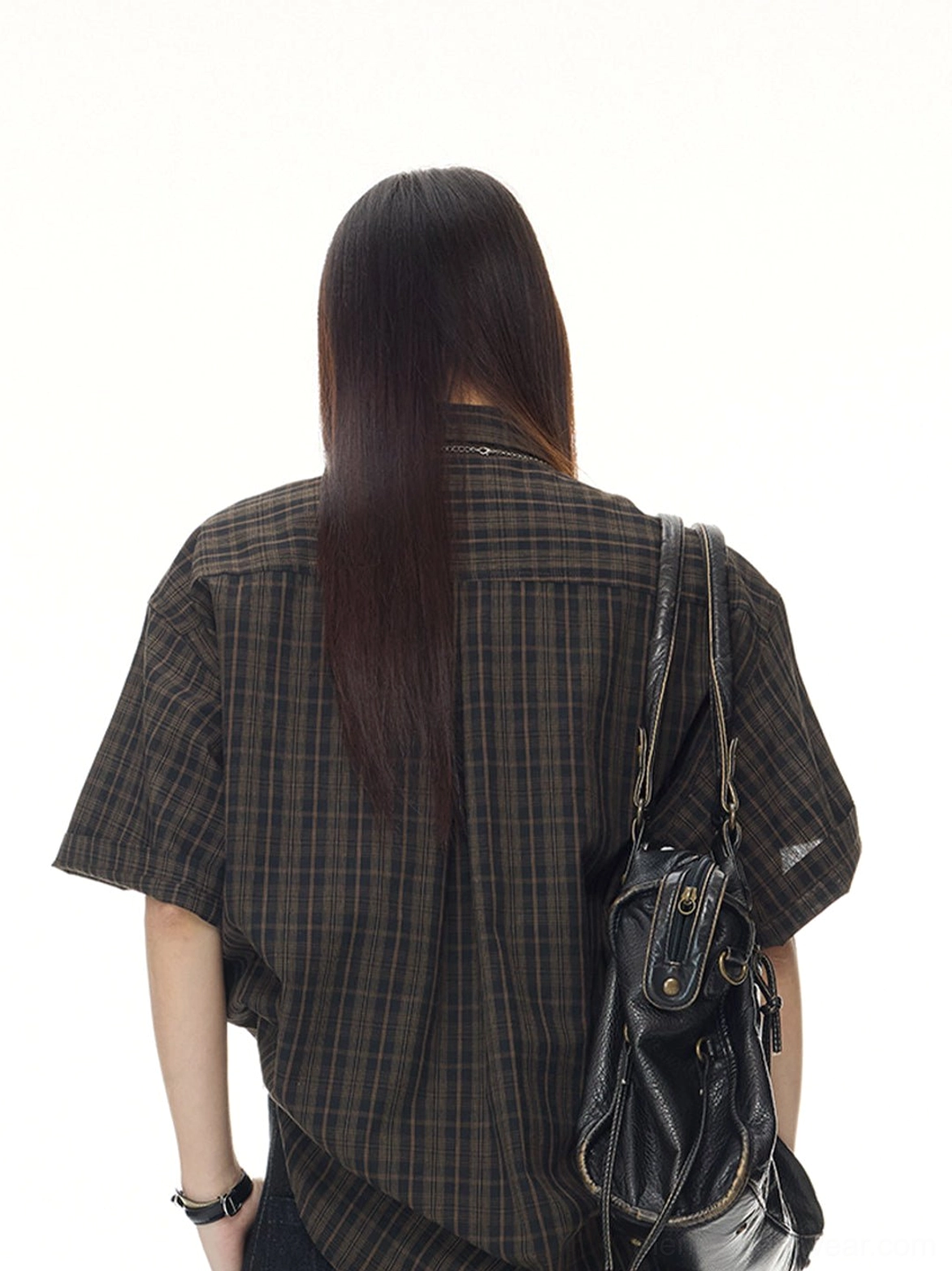 Rear view of a female model wearing a coffee plaid short sleeve shirt with a black leather shoulder bag and relaxed streetwear fit