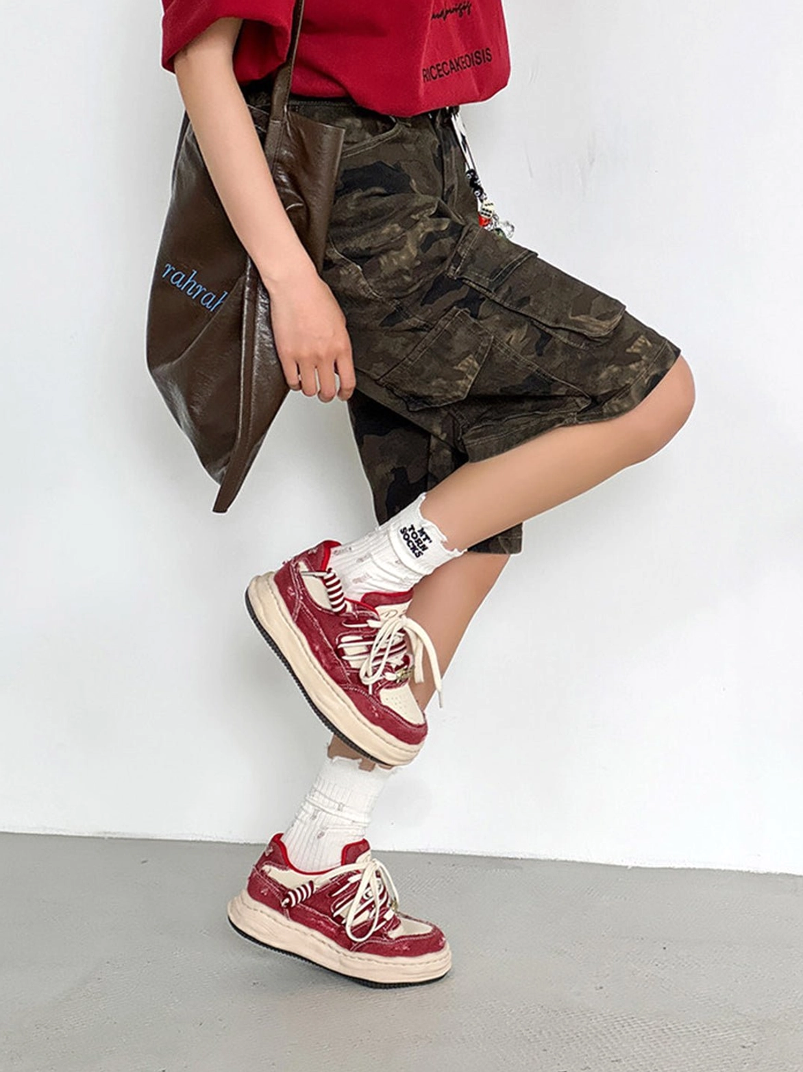 Red and cream vintage platform sneakers styled with a red cropped tee, camouflage cargo shorts, and a leather shoulder bag