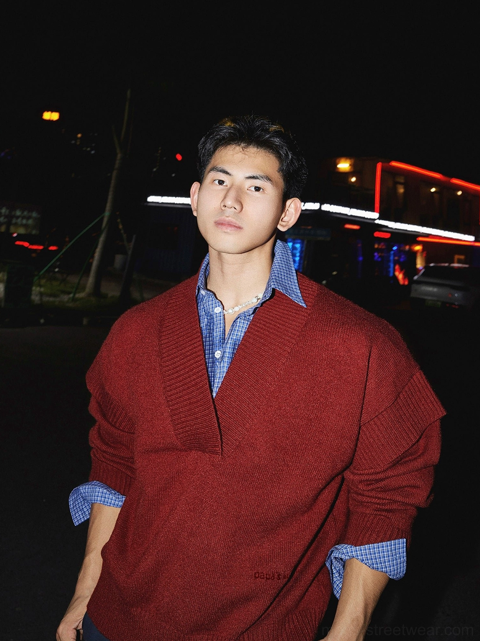 Close-up of red deep V-neck oversized knit sweater showing ribbed cuffs and blue checked shirt layering detail