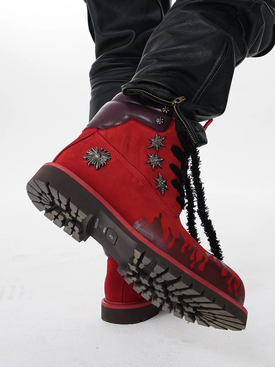 Angled view of red flame genuine leather combat boots showing deep tread lug outsole and metal studs