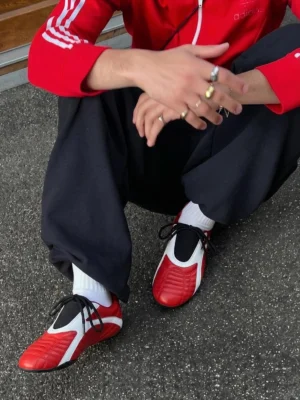 Red flat lace-up streetwear sneakers worn with a red track jacket loose dark sweatpants and white crew socks outdoors