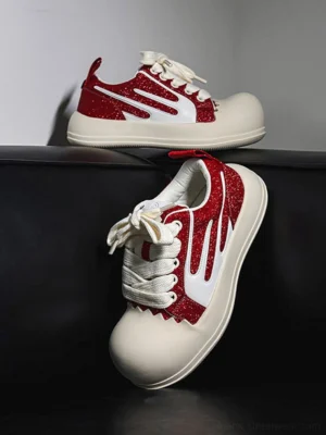 Red glitter stripe chunky platform sneakers with oversized white round toe caps displayed on a black leather sofa