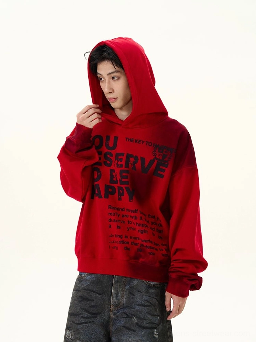 Left three-quarter front view of a red graphic oversized hoodie with black motivational slogan print, faded hem detail, ribbed cuffs, attached hood, and distressed dark jeans