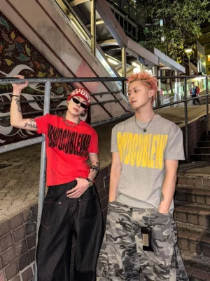 Red and gray graphic streetwear T-shirts worn with wide-leg black jeans and camouflage cargo pants in an urban night street setting