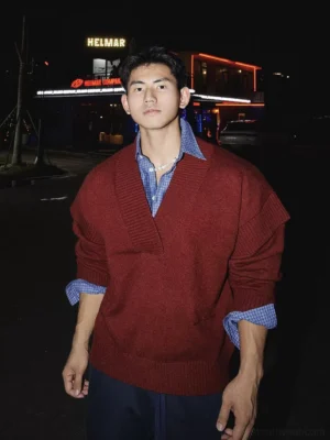Red oversized deep V-neck knit sweater layered over a blue checked shirt on a male model in a nighttime streetwear setting