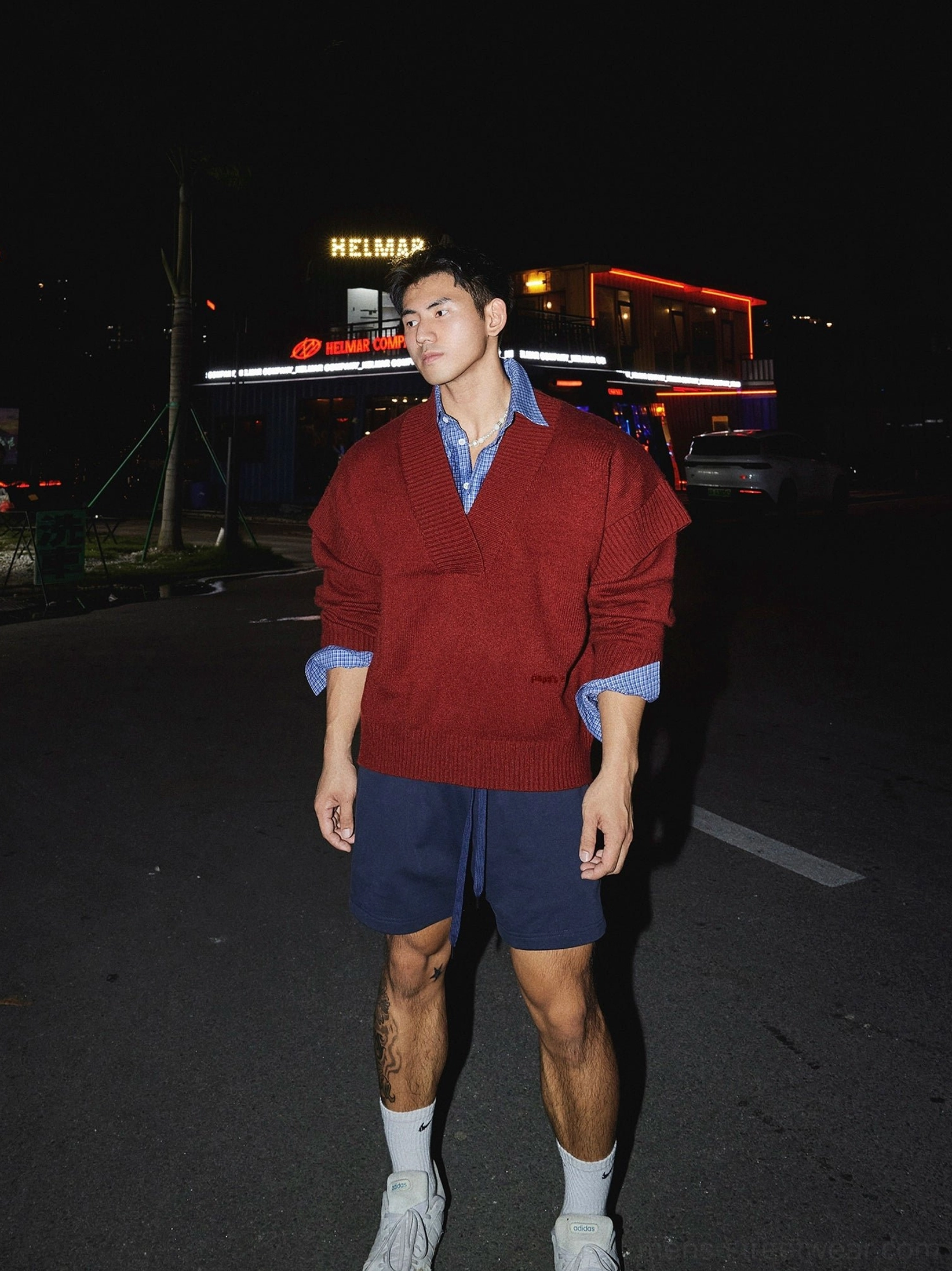Red oversized V-neck pullover sweater with blue checked shirt, navy shorts, white socks and sneakers