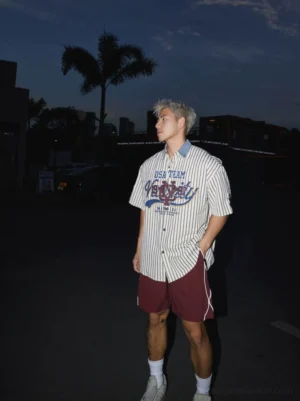 Red reflective stripe swim shorts styled with a striped graphic button-up shirt in a nighttime city streetwear outfit