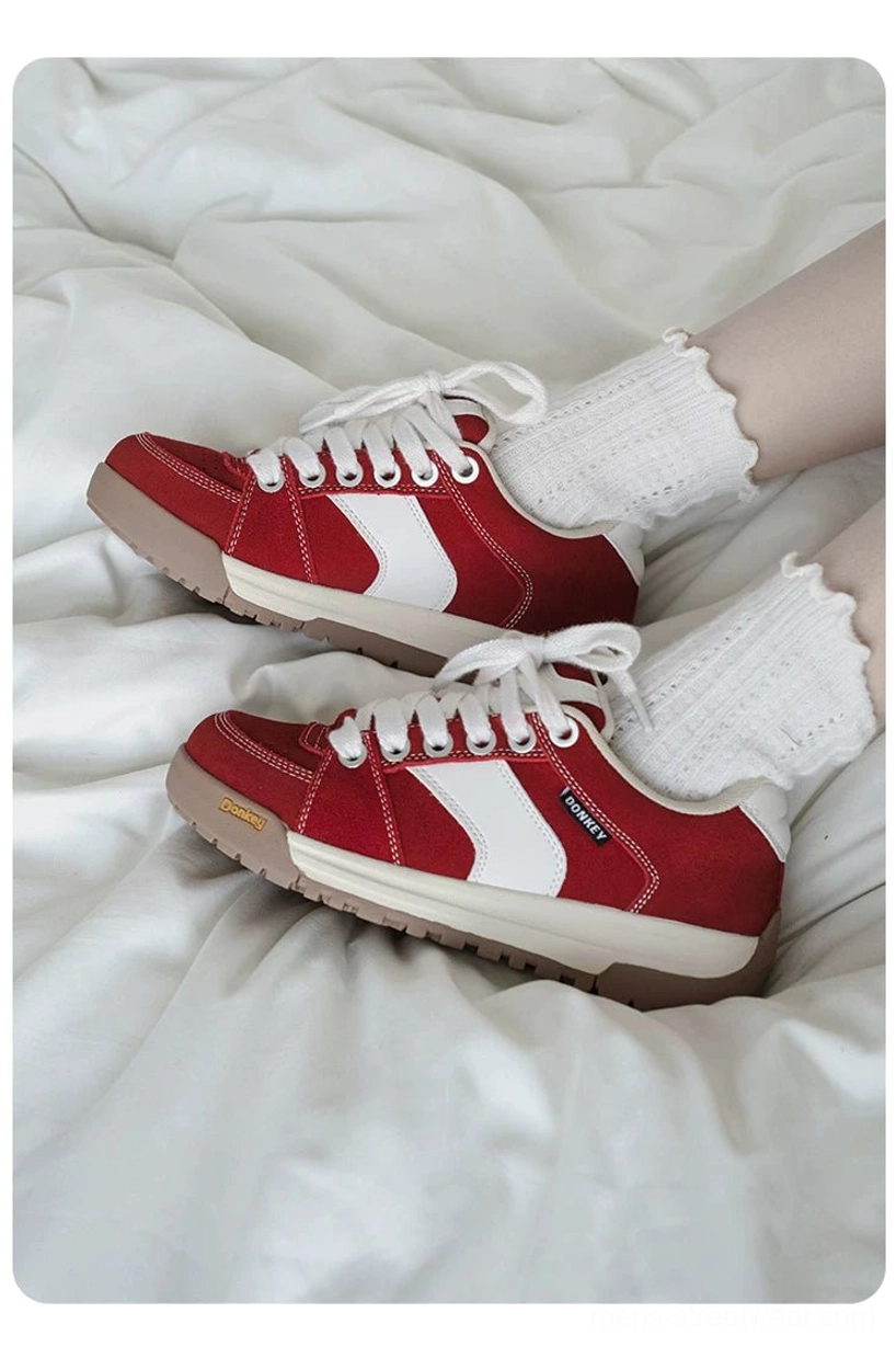 Pair of red suede retro court sneakers arranged on white bedding showing the full color-block silhouette and gum soles