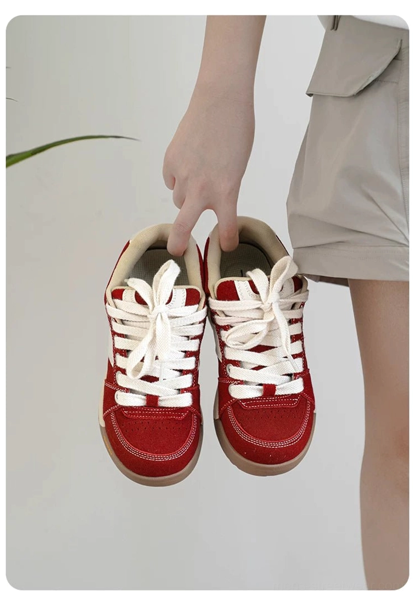 Pair of red suede court sneakers held from above with white contrast details and gum-colored rubber soles