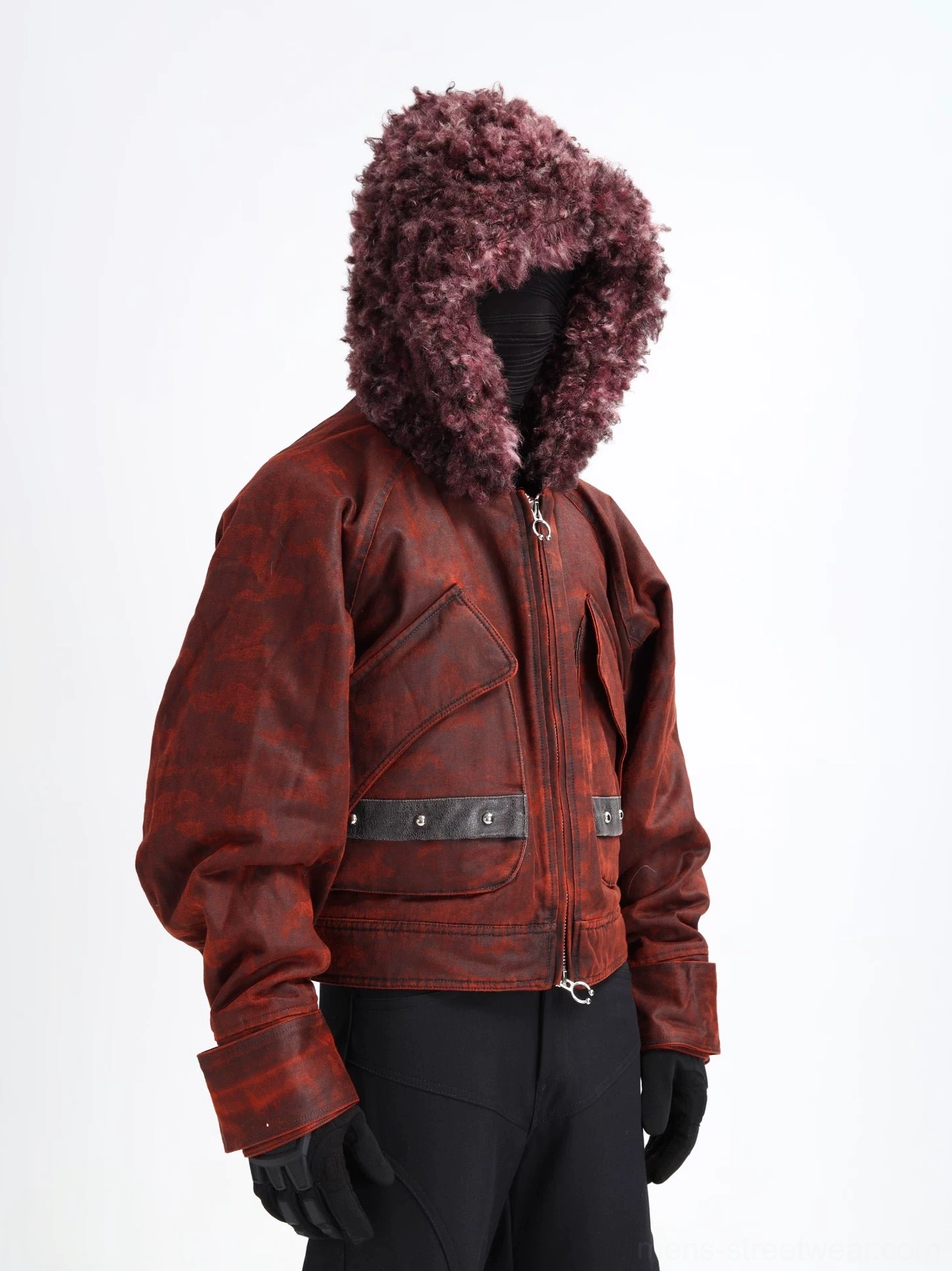 Reddish brown distressed camo faux shearling hooded cropped bomber jacket shown from the left front with oversized flap pockets, studded leather-look straps, metal zipper, and black streetwear trousers