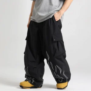 Black reflective flame print cargo snow pants shown from a low three quarter front angle with oversized wide legs, utility pockets, and yellow snow boots