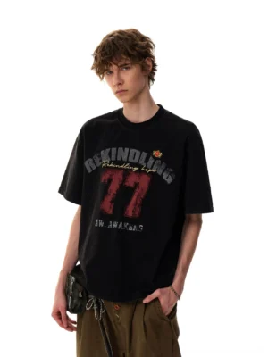 Model wearing a black Rekindling 77 vintage varsity graphic oversized streetwear T-shirt with wide-leg cargo pants and a crossbody bag