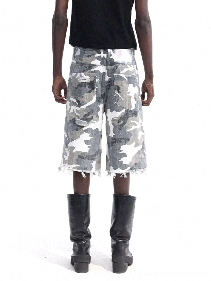 Rear view of relaxed camouflage denim cutoff shorts featuring a loose wide-leg silhouette, classic rear pockets, and frayed raw hem styled with a black cropped tank and mid-calf boots