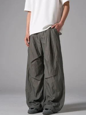 Side front view of relaxed crinkled wide-leg trousers showing waistband, vertical seam pleats and long loose legs