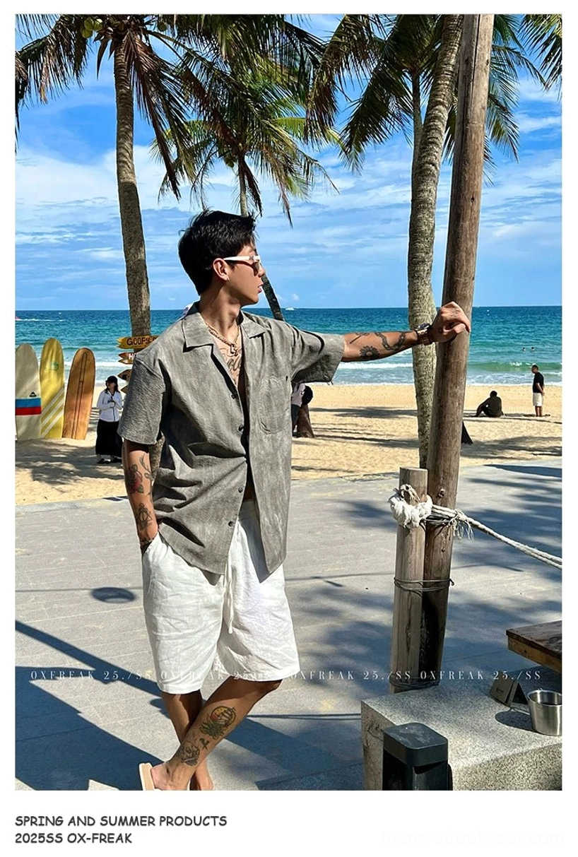 Relaxed grey-toned Cuban collar short sleeve shirt shown from the back on a coastal boardwalk with white shorts