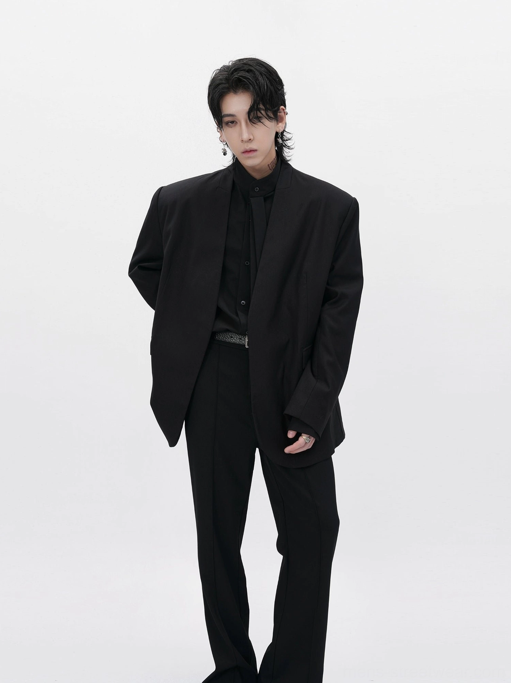 Three quarter side view of a relaxed-fit black collarless blazer with belted tailored trousers