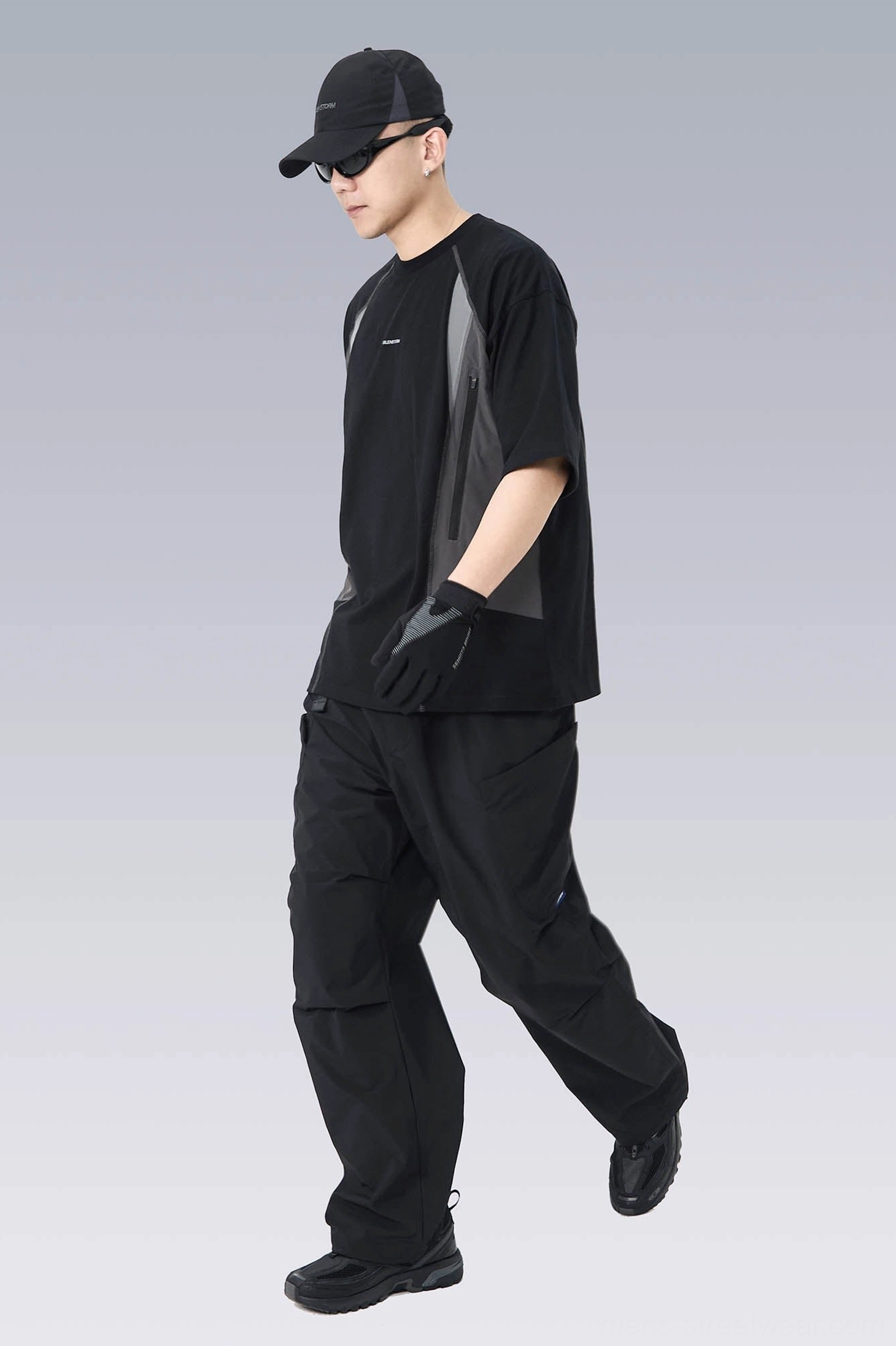 Walking profile of a relaxed oversized techwear T-shirt styled with black cargo pants, showing subtle side color-block details and loose sleeves