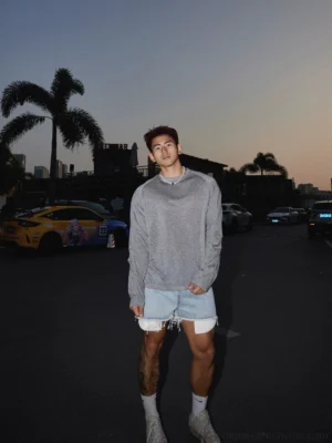 Full body three quarter view of relaxed light gray long sleeve streetwear tee styled with distressed denim shorts white socks and sneakers