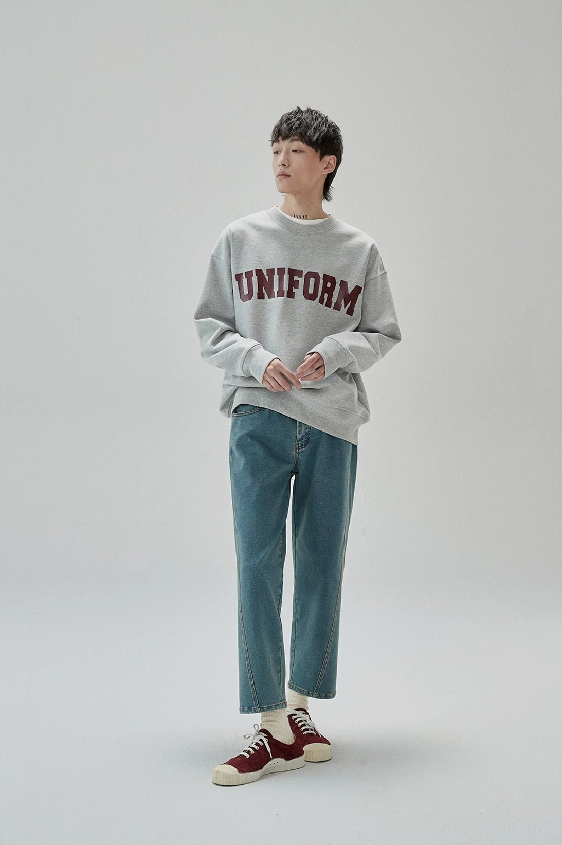 Side view of relaxed gray graphic crewneck sweatshirt with ribbed cuffs and collegiate UNIFORM chest print