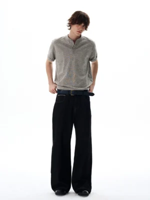 Male model wearing heather grey short sleeve Henley knit shirt with black wide-leg trousers in a minimalist studio