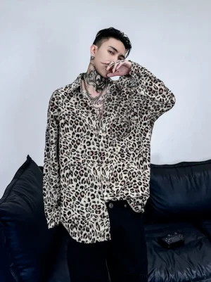 Three-quarter front view of a tattooed male model wearing a relaxed oversized leopard print satin shirt with long sleeves in a modern streetwear setting