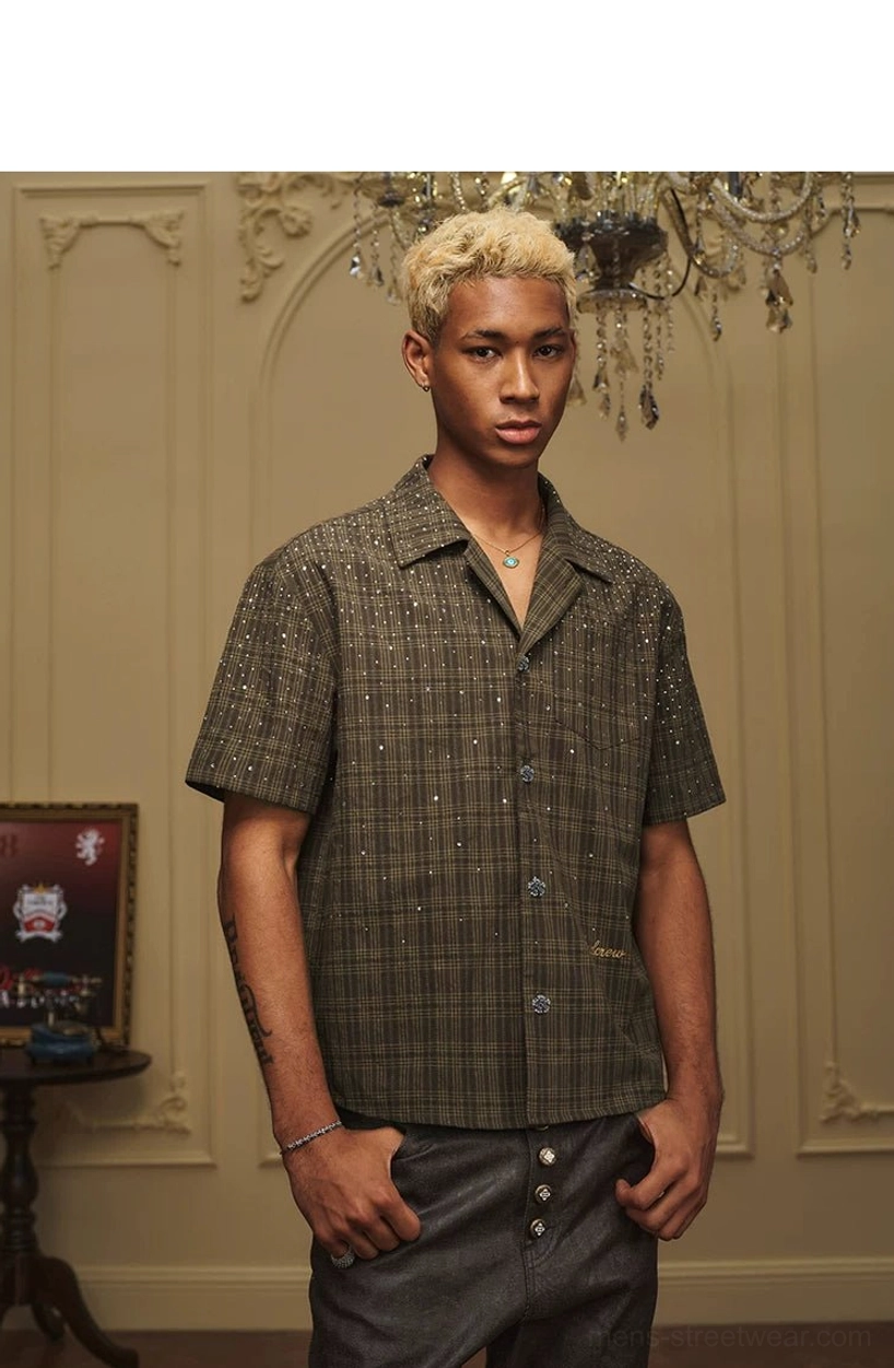 Male model wearing a relaxed olive green plaid camp collar shirt with decorative buttons and loose streetwear fit