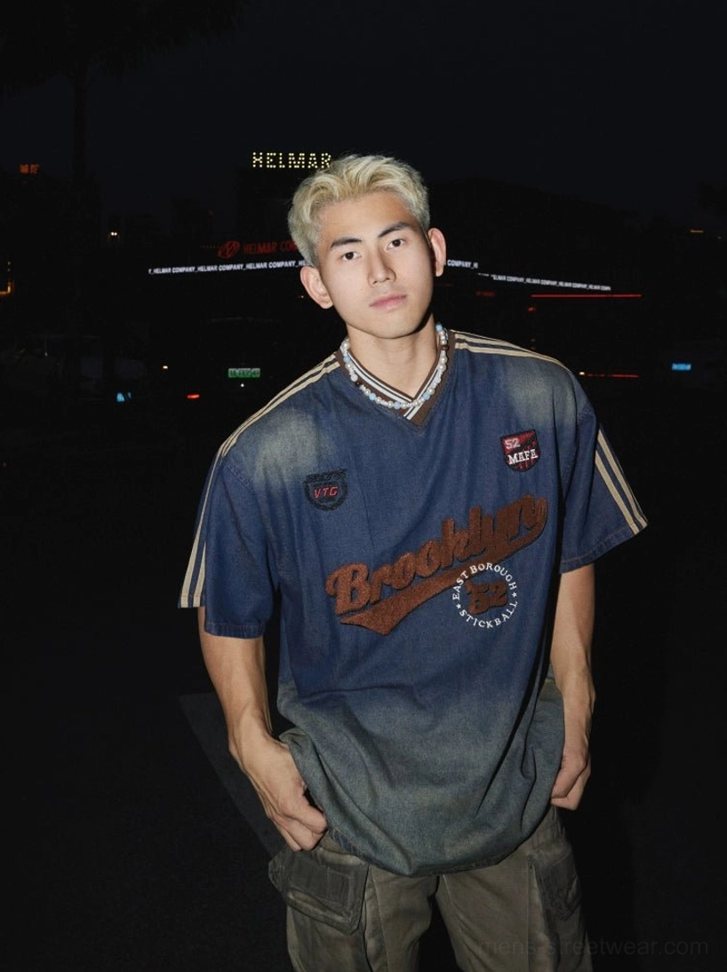 Front medium shot of a relaxed oversized blue Brooklyn varsity streetwear T-shirt with faded denim wash, embroidered chest lettering, and vintage athletic patches