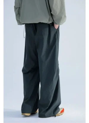 Rear view of relaxed pleated track pants showing elastic drawstring waist, back pleats, wide-leg fit, and adjustable cuffs