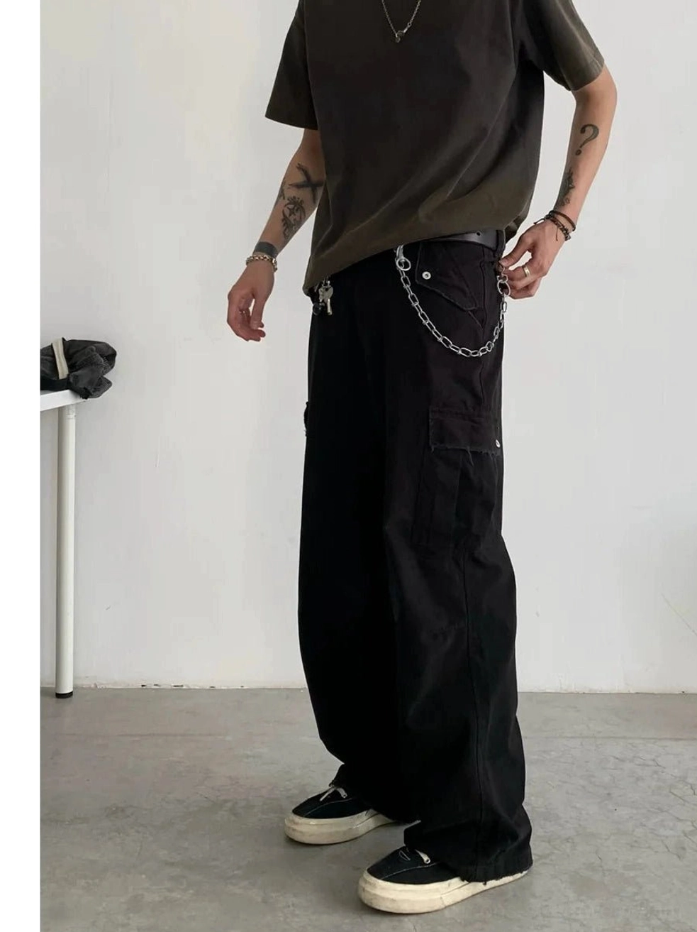 Front full-body view of relaxed straight leg cargo pants in a dark neutral tone with multiple flap pockets and pant chain detail styled with a brown streetwear tee and sneakers