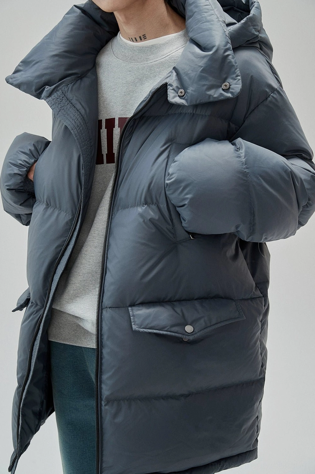 Side upper-body view of relaxed graphic sweatshirt layered beneath a long dark gray down jacket