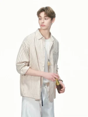 Light khaki vertical stripe oversized shirt shown from a three-quarter front view with rolled sleeves, chest patch pocket, white T-shirt, and relaxed white trousers