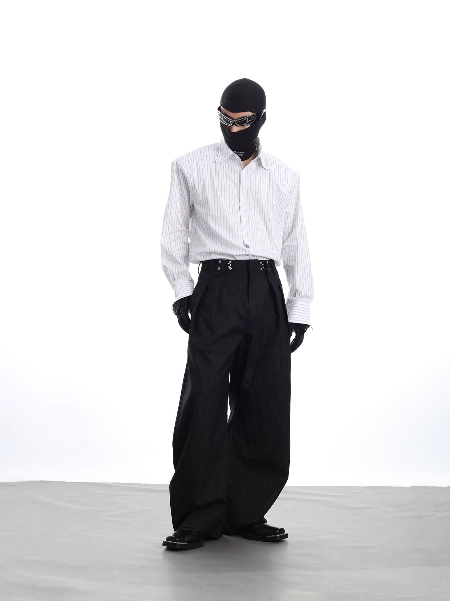 Side view of a relaxed fit vertical stripe long sleeve shirt paired with black pinstripe wide-leg trousers and urban accessories