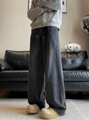 Relaxed wide-leg black streetwear sweatpants modeled indoors with oversized side pockets, structured seams, drawstring waist, gray zip-up sweatshirt, and beige platform loafers