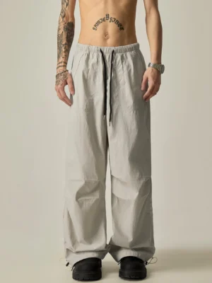 Front view of relaxed wide-leg drawstring cargo track pants in light silver gray crinkled fabric with elastic waist and adjustable ankle cuffs