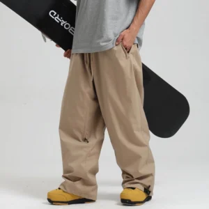 Khaki relaxed wide-leg waterproof snow pants styled with yellow ski boots and a snowboard for streetwear riding