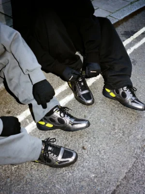 Retro colorblock low-profile sneakers worn with Korean streetwear outfits on an urban road, featuring black mesh, gunmetal grey panels, neon yellow accents, and a slim outsole