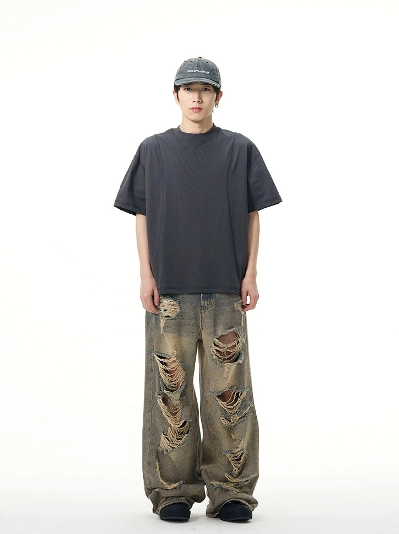 Male model wearing retro blue distressed wide-leg ripped jeans with oversized dark gray t-shirt and black shoes