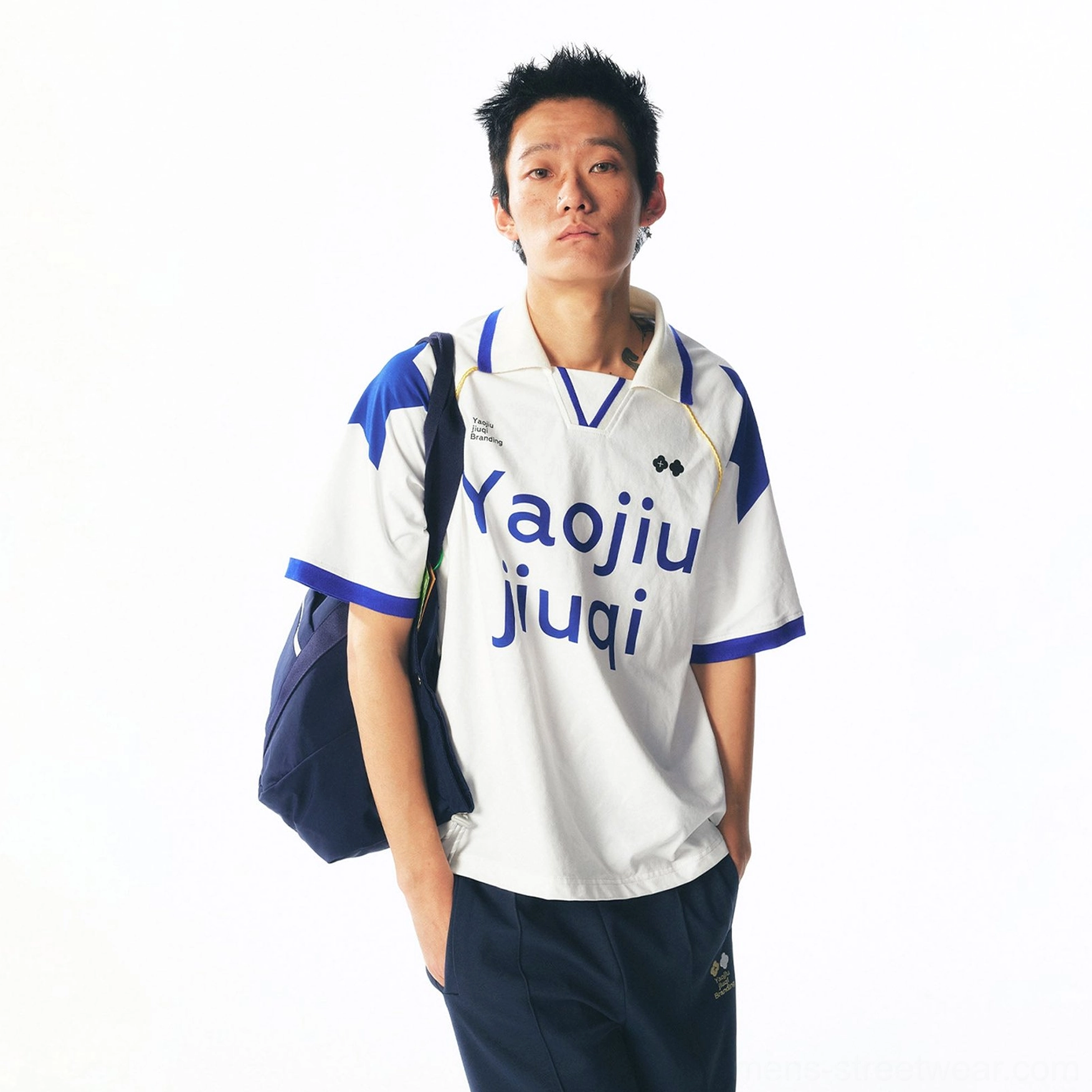 Side back view of a blue-trimmed retro football jersey with contrast shoulder panels, bold front typography, and a navy streetwear shoulder bag