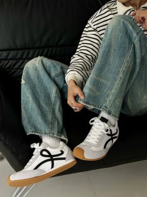 Male model wearing retro casual panel sneakers with white socks, striped top, and ripped jeans in a relaxed streetwear outfit