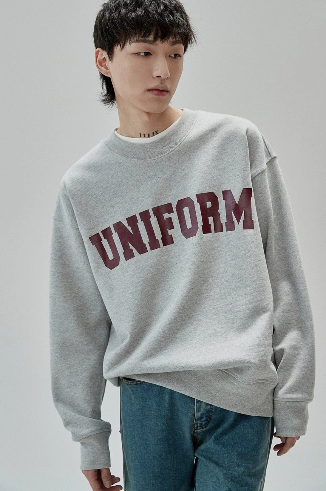 Heather gray UNIFORM graphic crewneck sweatshirt worn with straight blue jeans in relaxed Korean streetwear style