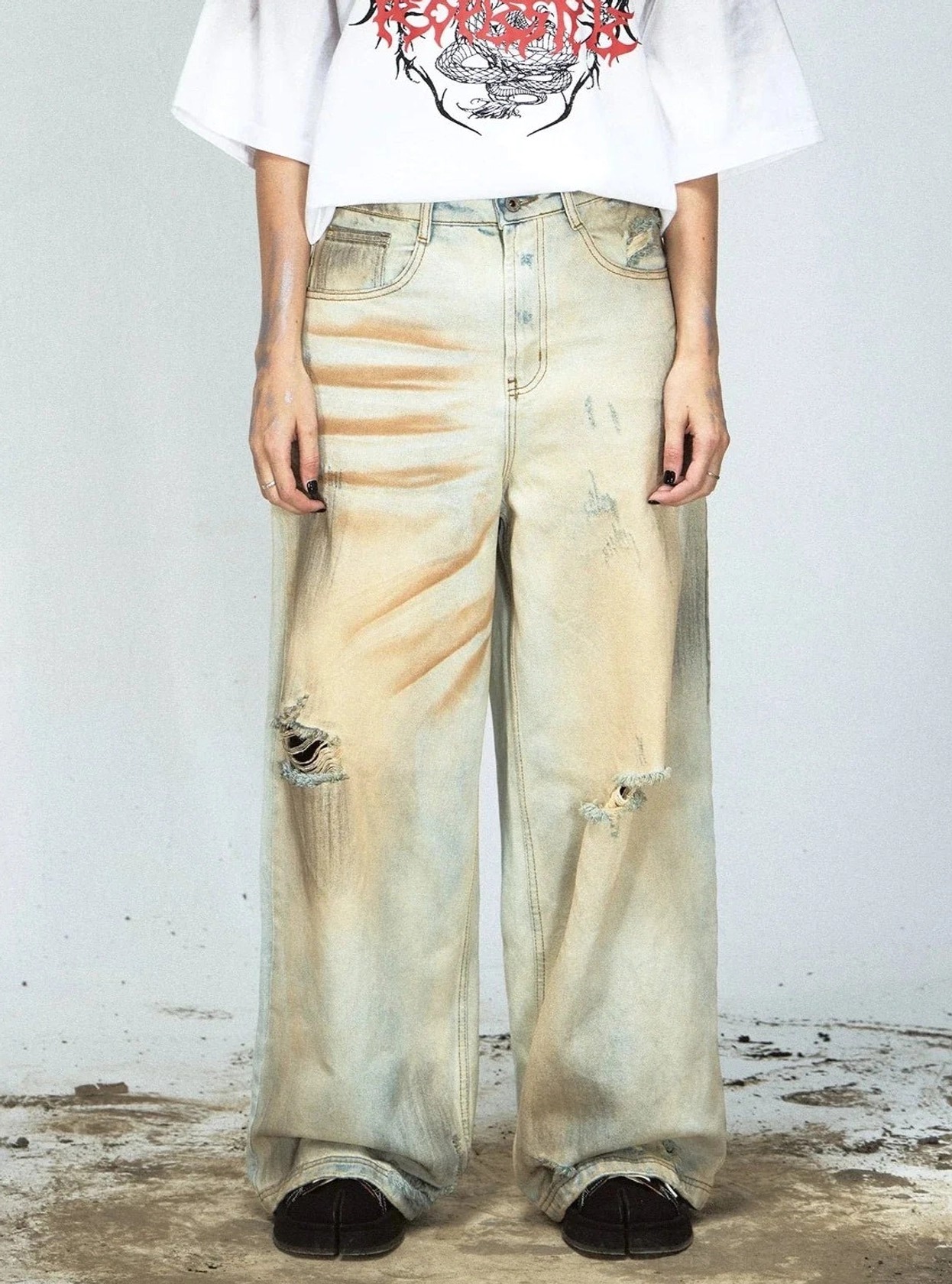 Front styling view of yellow tinted distressed denim jeans with bilateral knee rips and graphic T-shirt
