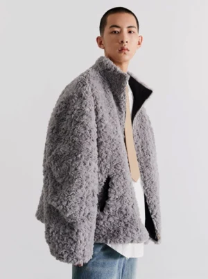 Grey sherpa side of reversible oversized bomber jacket shown in front three-quarter view with blue denim jeans
