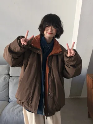 Model wearing reversible brown oversized padded jacket with stand collar in minimalist indoor studio front three quarter view